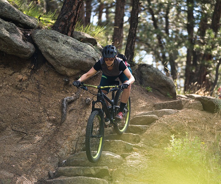 person riding a mountain bike down stone steps, on a trail in the woods 