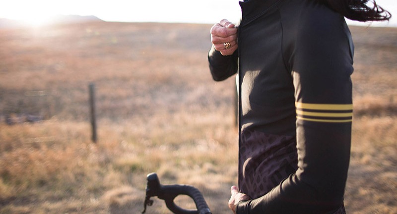 A close up of a person standing in a field and zipping up a long sleeved jersey