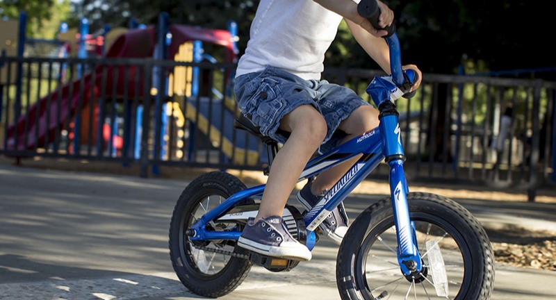 A kid riding his bike in front of a playground.