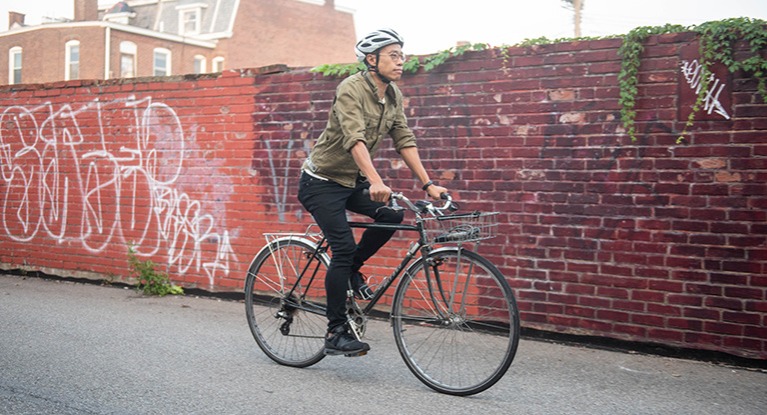 man riding a single speed bike with a basket on the front in a downtown setting.