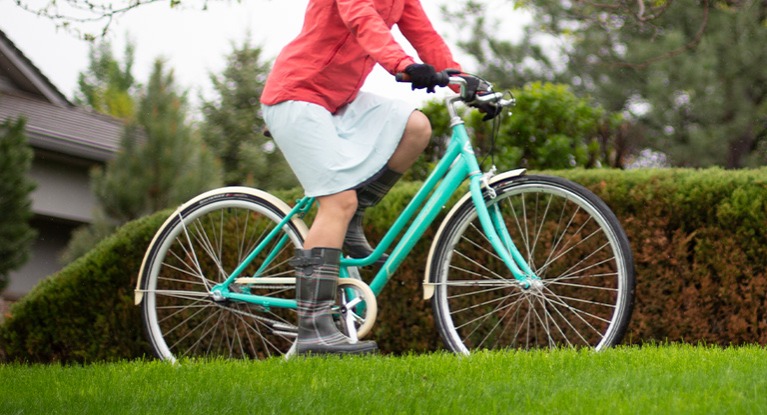 woman on a green cruiser bike wearing a dress and rainboots