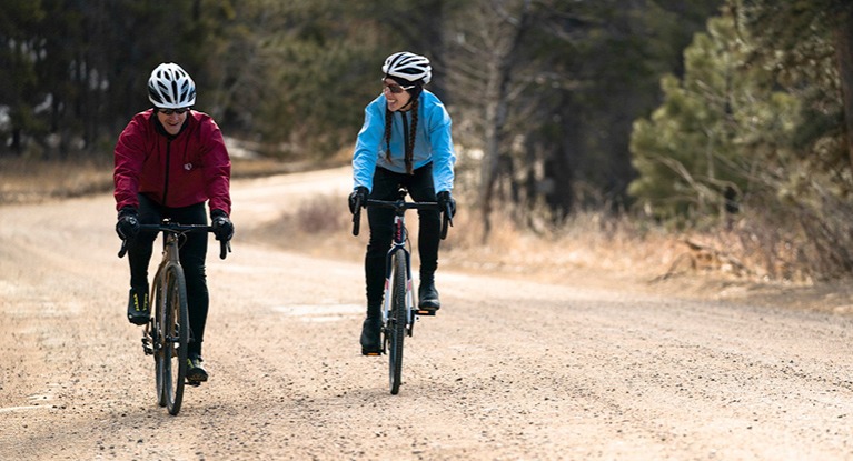 Two friends laughing and riding bikes on a gravel road.