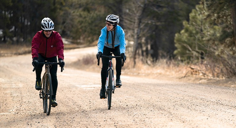 A man and a woman riding on a gravel road.