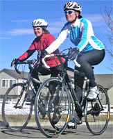 Two women riding their bikes next to each other in cold weather.