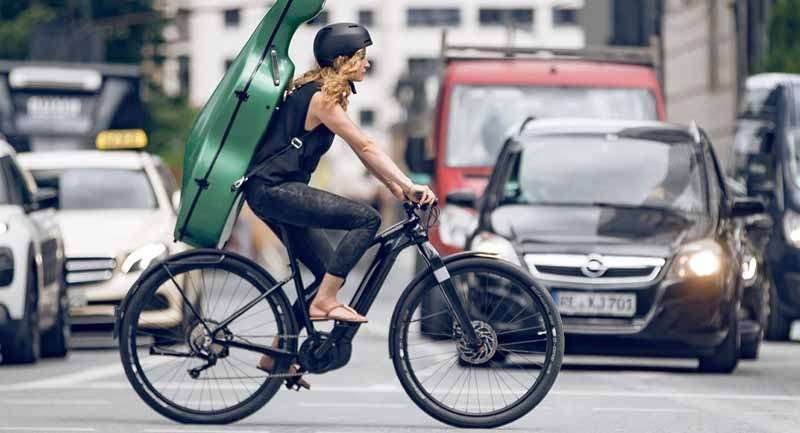 A woman with a guitar riding a black Cannondale electric bike in the city