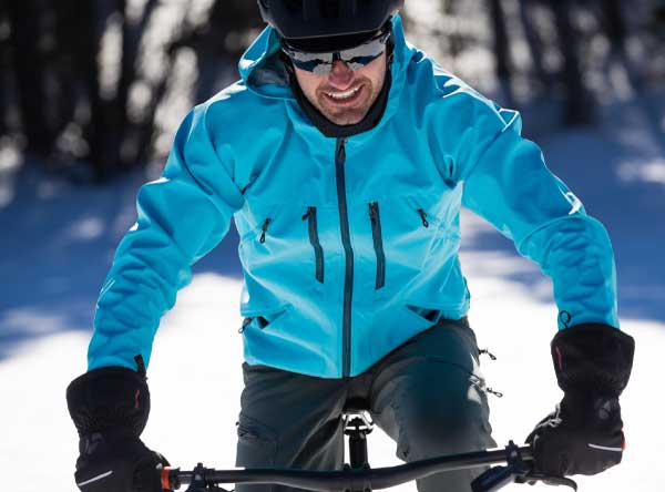 "man riding bike in snow with gloves and jacket"