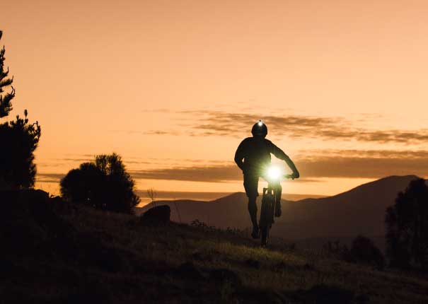 "cyclist riding at sunset with bright headlight"