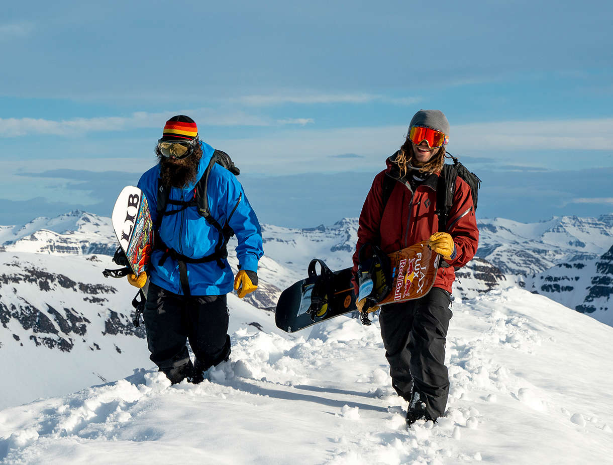 Image of two people on top of a snowy mountain holding snowboards