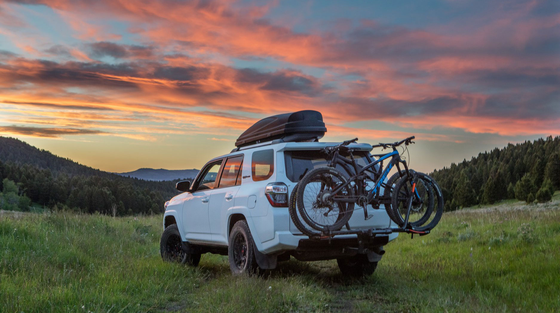 SUV with hitch rack and two mountain bikes at sunset