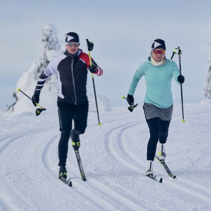 two xc skiers skiing classic style in machined track