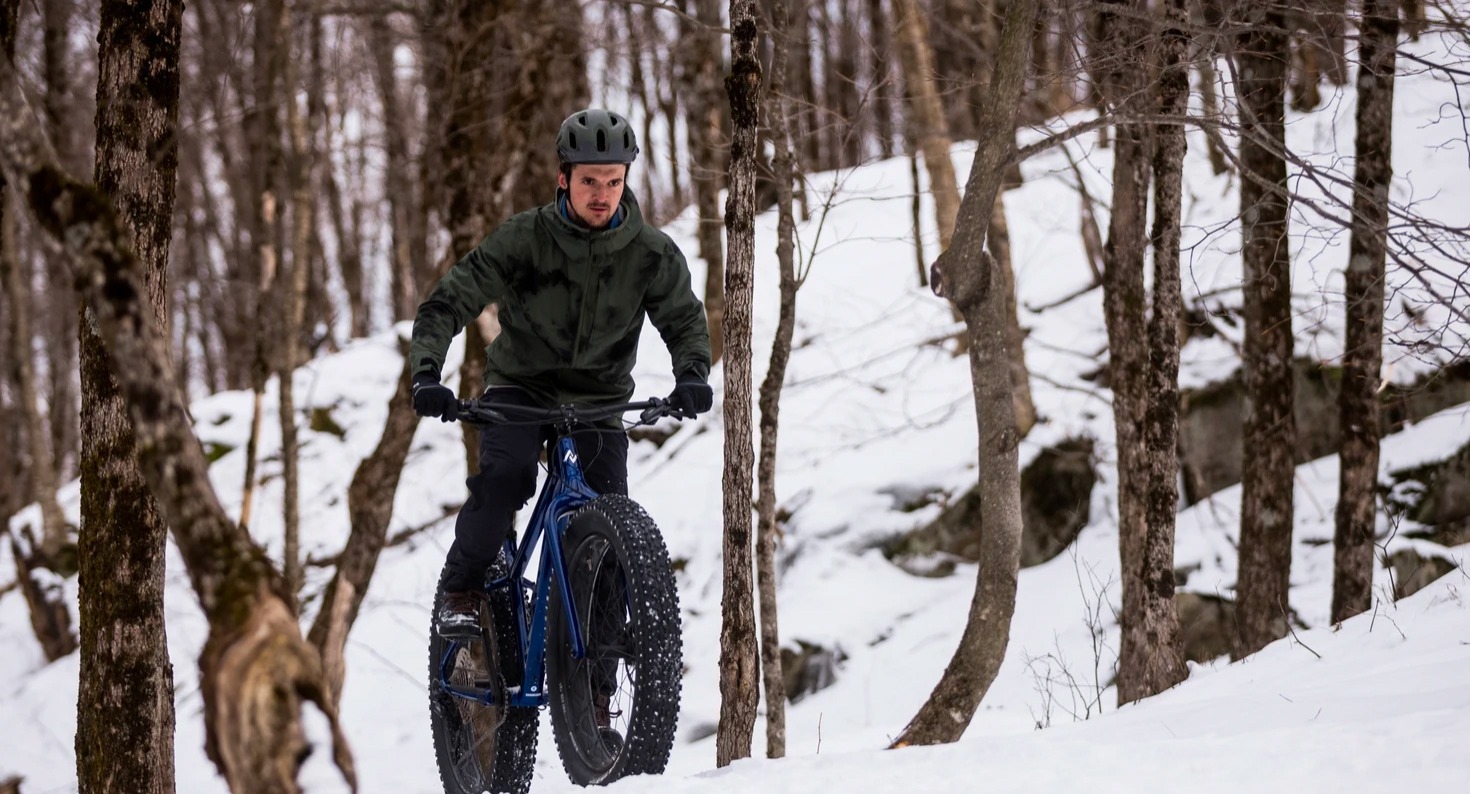 cyclist riding a fat bike over snow in the woods