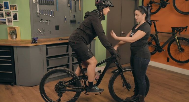 Two women adjusting sag on a full-suspension bike