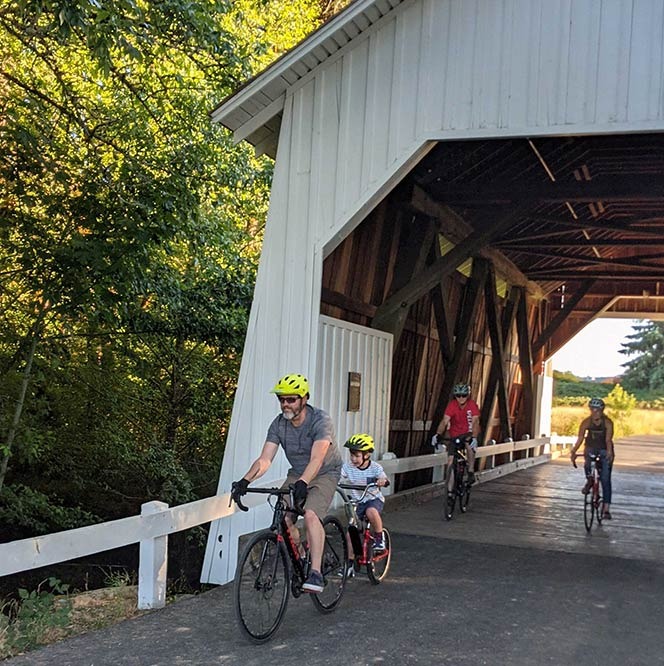Several people riding bikes through a covered bridge