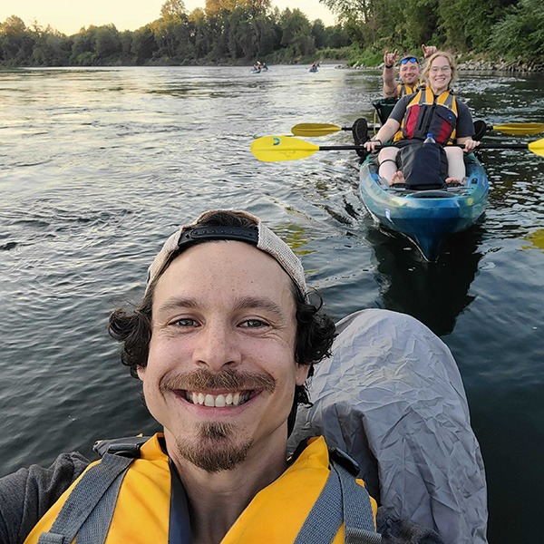 Man in life vest with several people in kayaks behind him on the water