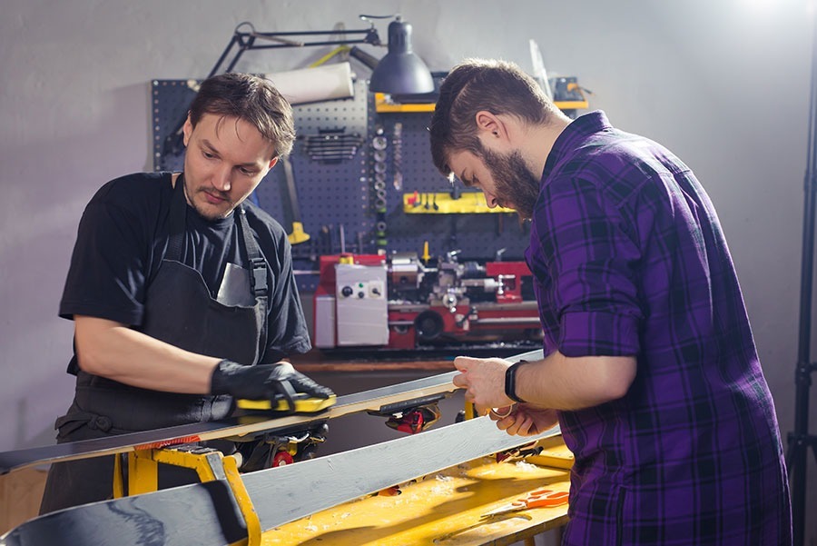 Two men in a ski workshop working on a pair of skis.