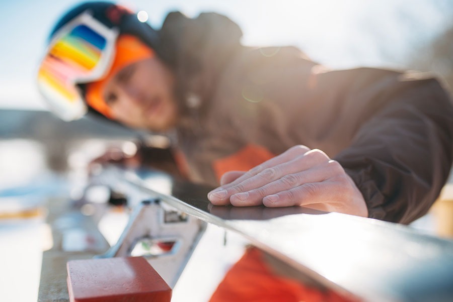 Man in ski gear inspecting the base of his ski.