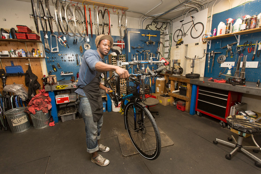 Man putting a bike on a repair rack inside a shop.