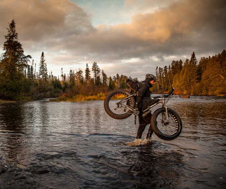 Person carrying their bike across a river
