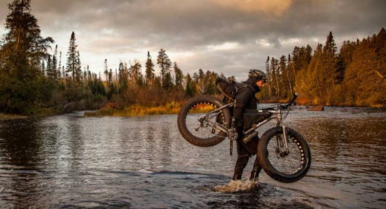 Bike Rentals | Image of a person carrying their bike across a river