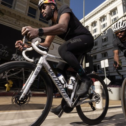 A man riding a silver Specialized road bike through a city street.