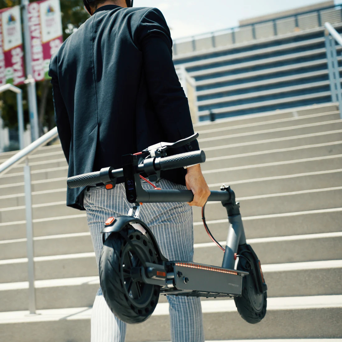 A man walking away with a Hiboy scooter in hand, folded up to carry up stairs.