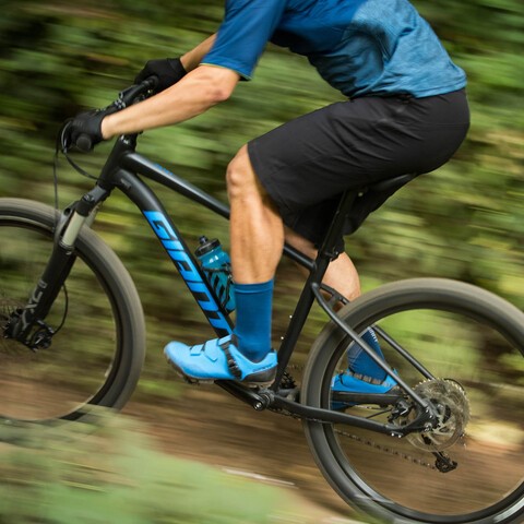 Close-up of a man riding a Giant mountain bike uphill through a wooded area.