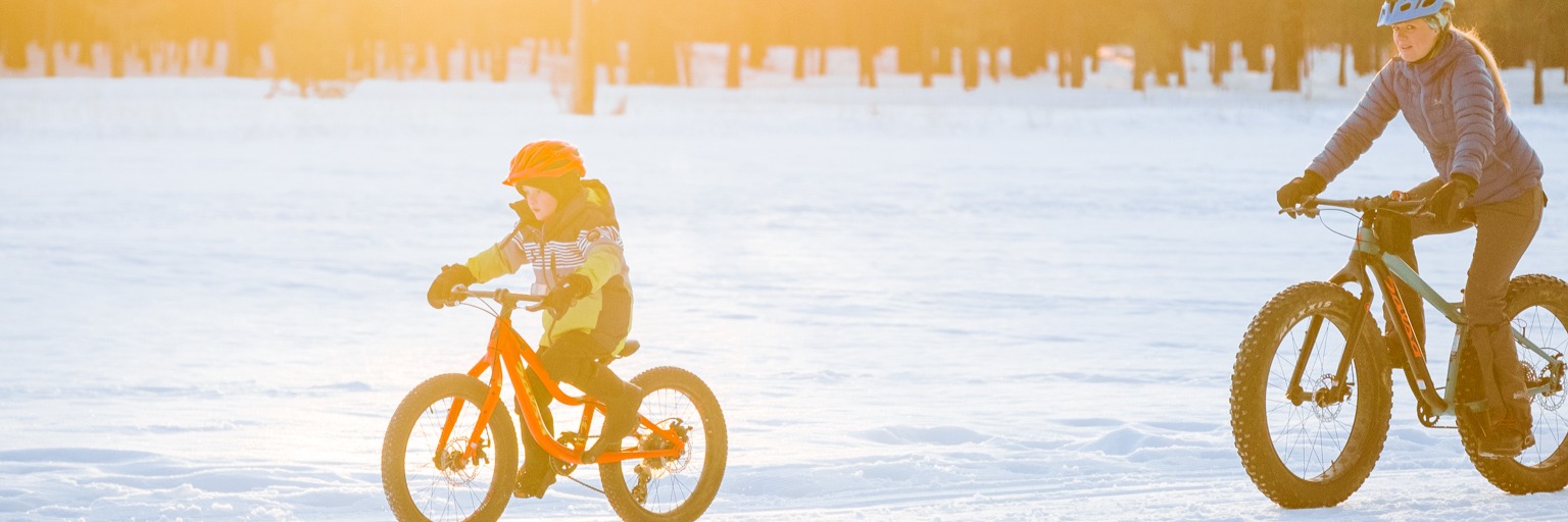 Image of a woman riding with her child on fat bikes in the snow