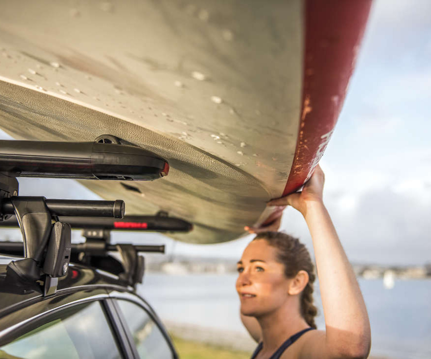 Woman loading a paddle board on to her car rack.