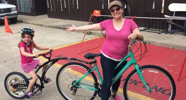 A mom and her kid riding on a bike and tag along bike