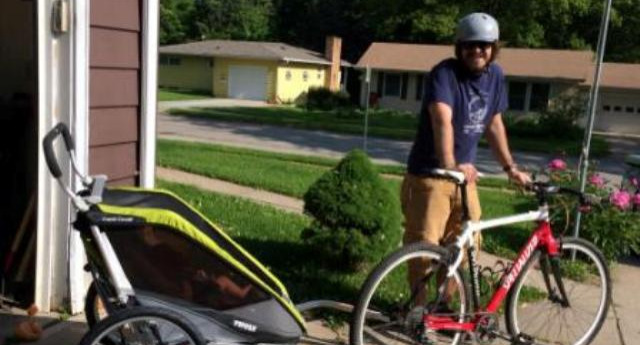 A man posing with a bike and trailer attachment 