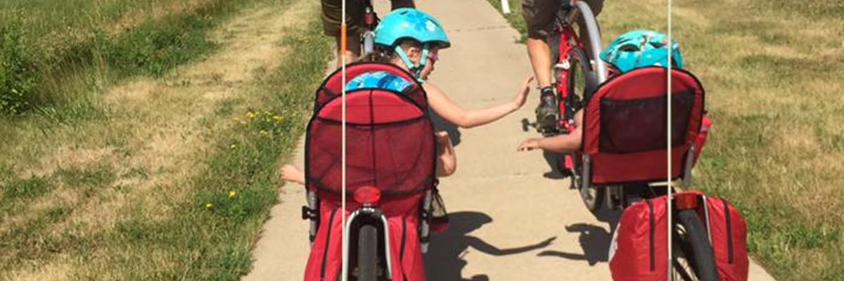 Two kids high-fiving while riding in trailers behind bikes