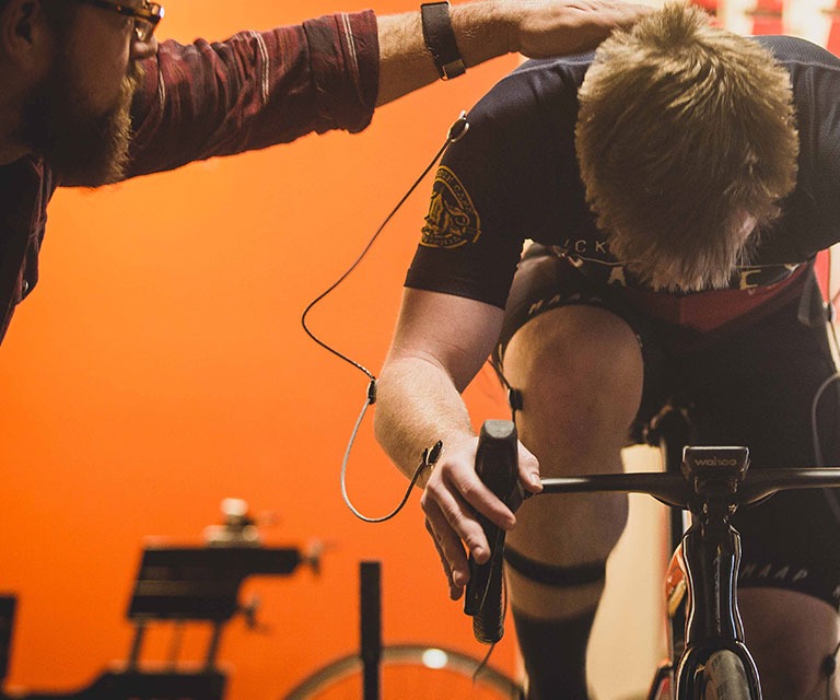 Male cyclist on an indoor trainer during a Retul bicycle fitting at Reser Bicycle Outfitters. Fit specialist evaluates riding biomechanics.