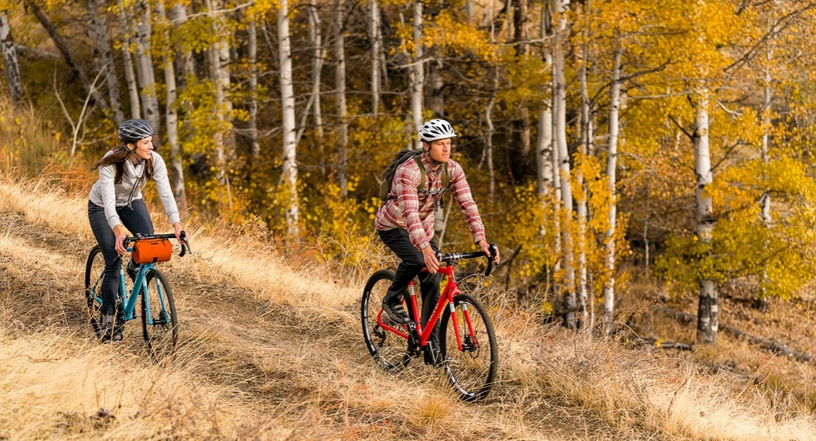 A man and woman ride Raleigh bikes near a fall forest