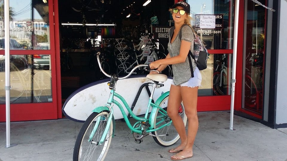 Woman with teal cruiser bike with surfboard racks