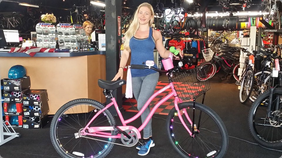 Pink cruiser bike with basket, bell, rim lights, and drink holder
