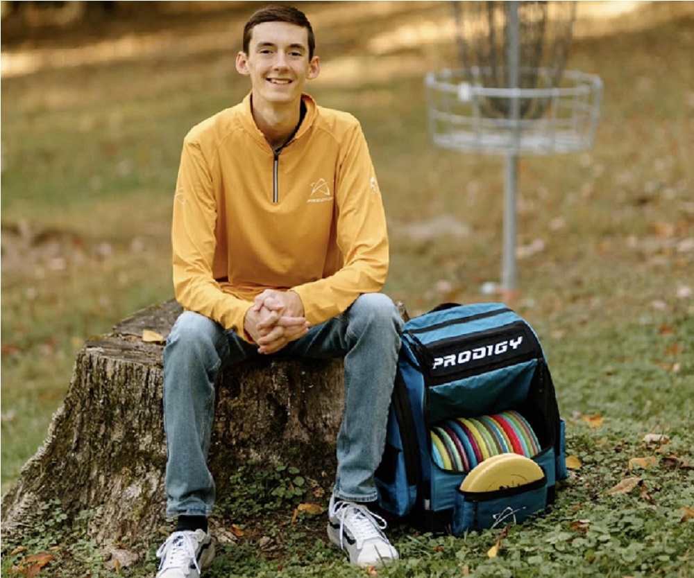 Man posing with disc golf discs in front of a disc golf goal