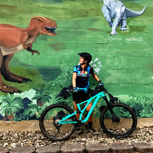 Woman with mountain bike posing in front of dinosaur mural