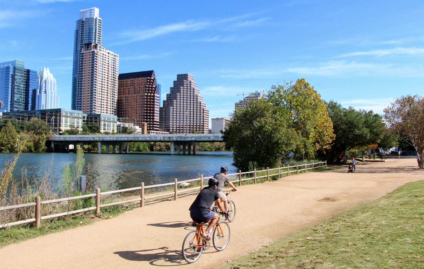 cyclists on crushed granite path along Lady Bird Lake with downtown Austin view