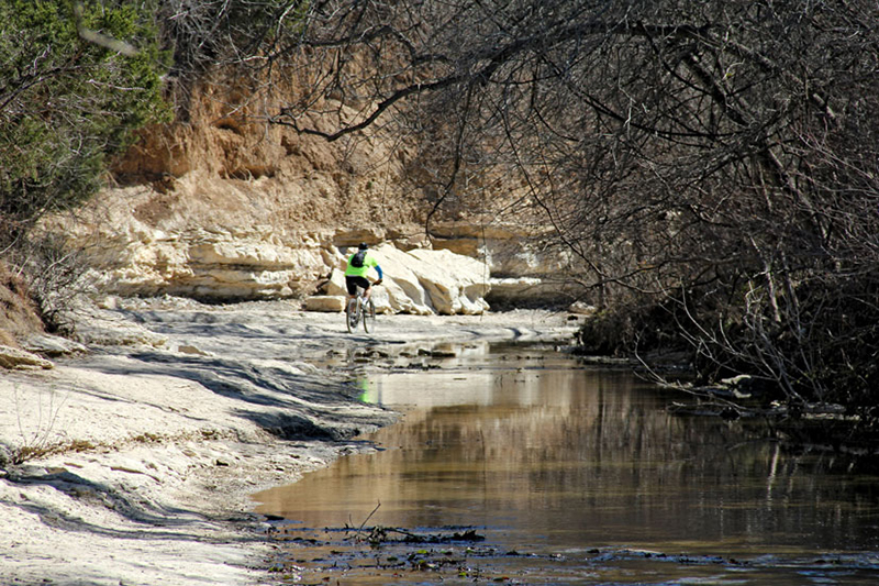 mountain biker rides along creekbed with limestone bluffs reflected in creek