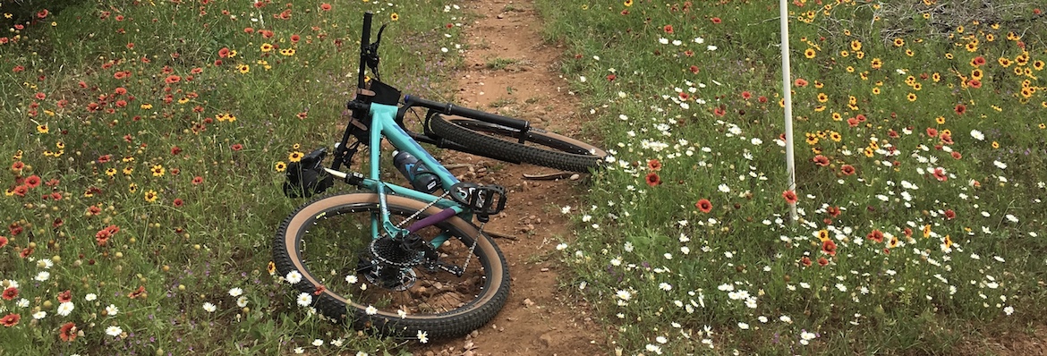 Kona mountain bike on trail surrounded by wildflowers