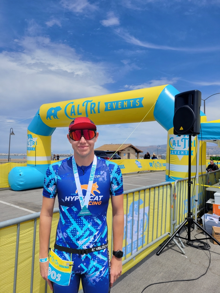 Male Hypercat Racing athlete poses next to the Cal Tri Events start/finish area