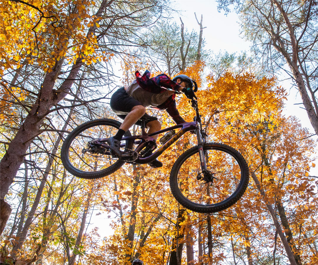 Mountain bike rider going over a jump in the woods in autumn