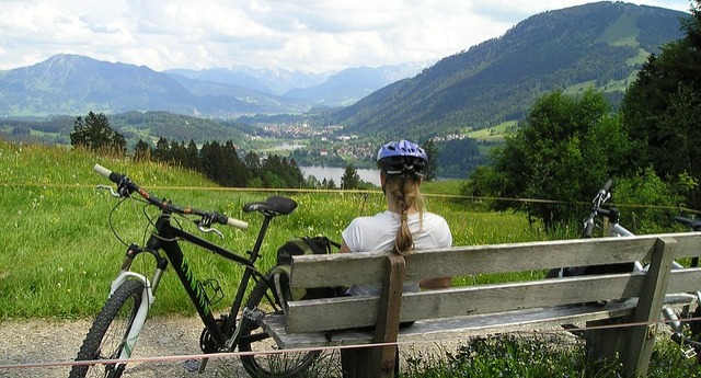woman bike riding sitting on a bench overlooking a mountain lake