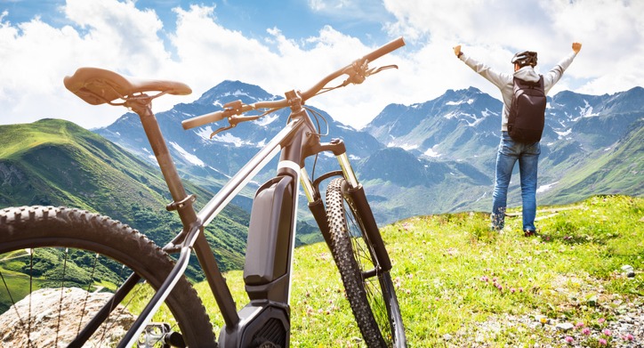 Cyclist standing in the mountains with his hands raised and his mountain e-bike near him