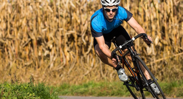 cyclist on a road bike banking around a turn with a cornfield in the background