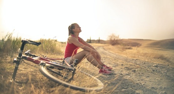 young lady sitting next to a dirt path outdoors with her gravel bike next to her