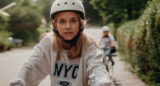 young girl wearing a bike helmet with an NYC sweatshirt riding her bike