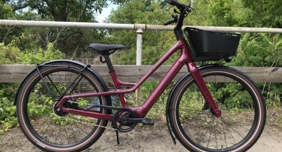 red ebike with a front basket, outside in front of a bridge railing