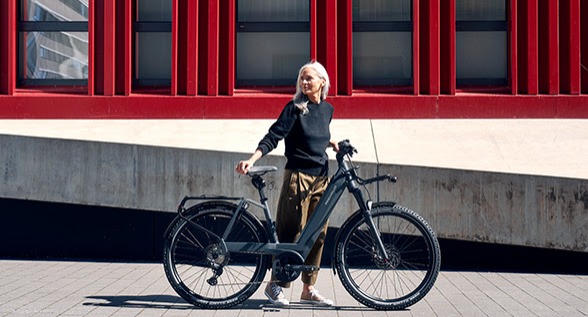 Woman standing behind an electric bike in front of a red fence