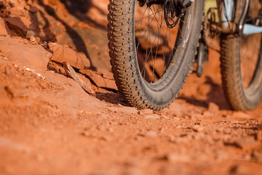 Closeup of bottom half of tires on a bike riding over red dirt